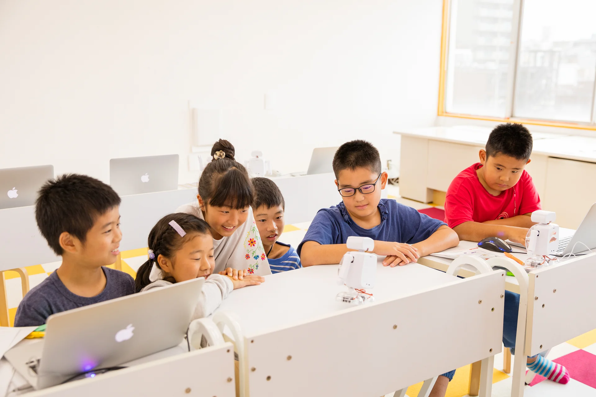 机に並んで座る子どもたちとノートパソコンでの学習風景